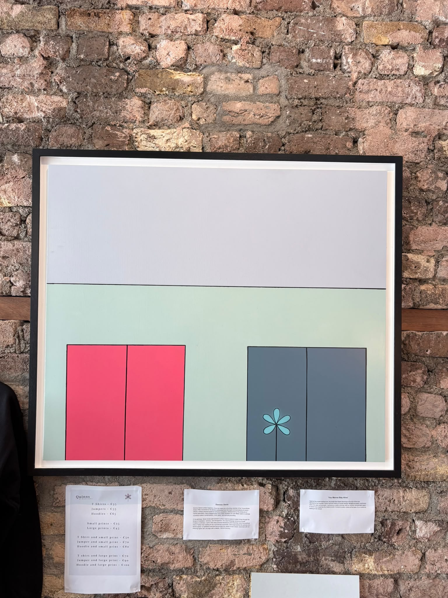 'You Wanna Stay Alive' by Dominic Denis - framed painting on the brick wall at Quinn's: a pale facade with red and grey doors, a single blue flower at the foot of one door